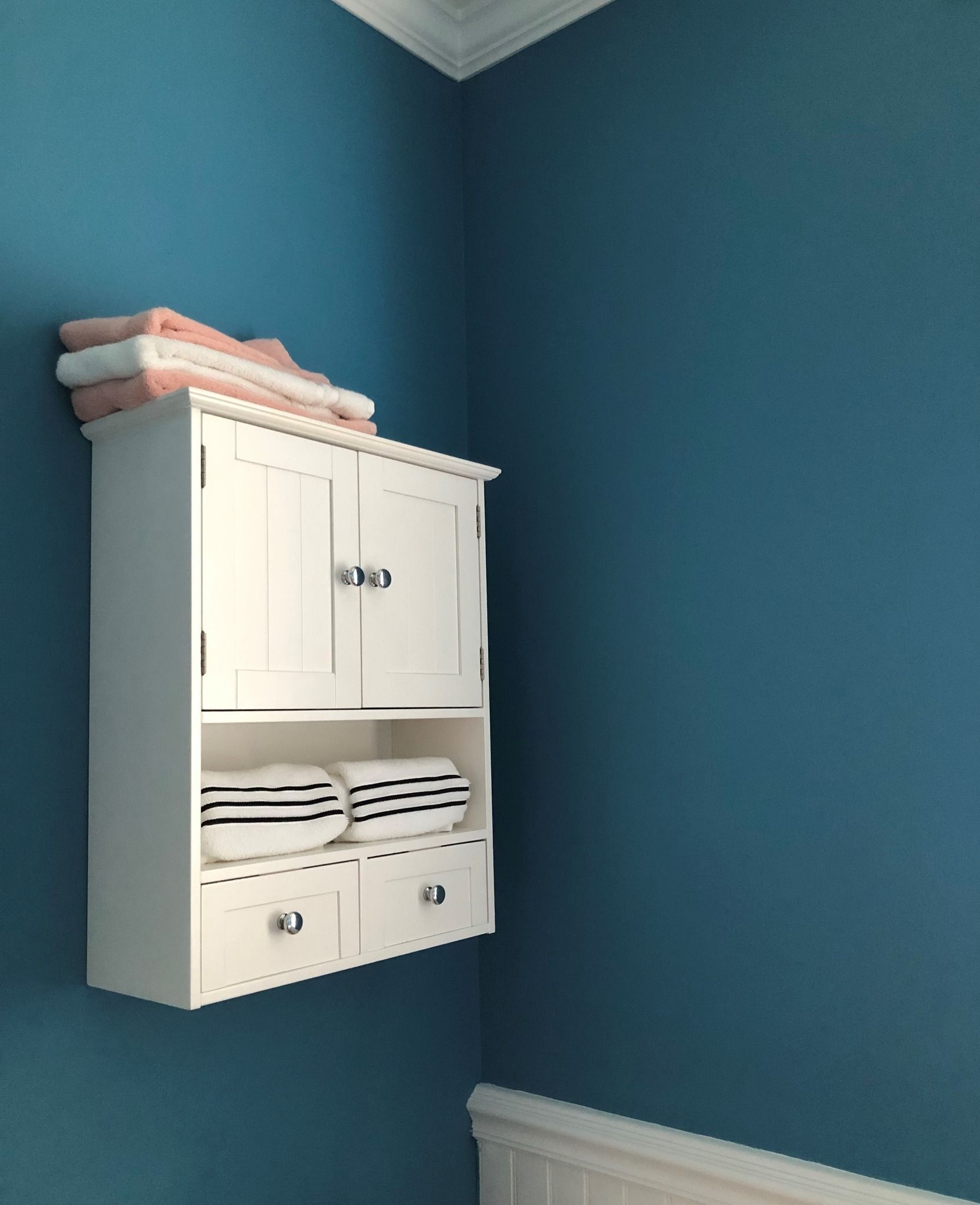 White bathroom cabinet on a teal wall, with towels stacked on top and inside.