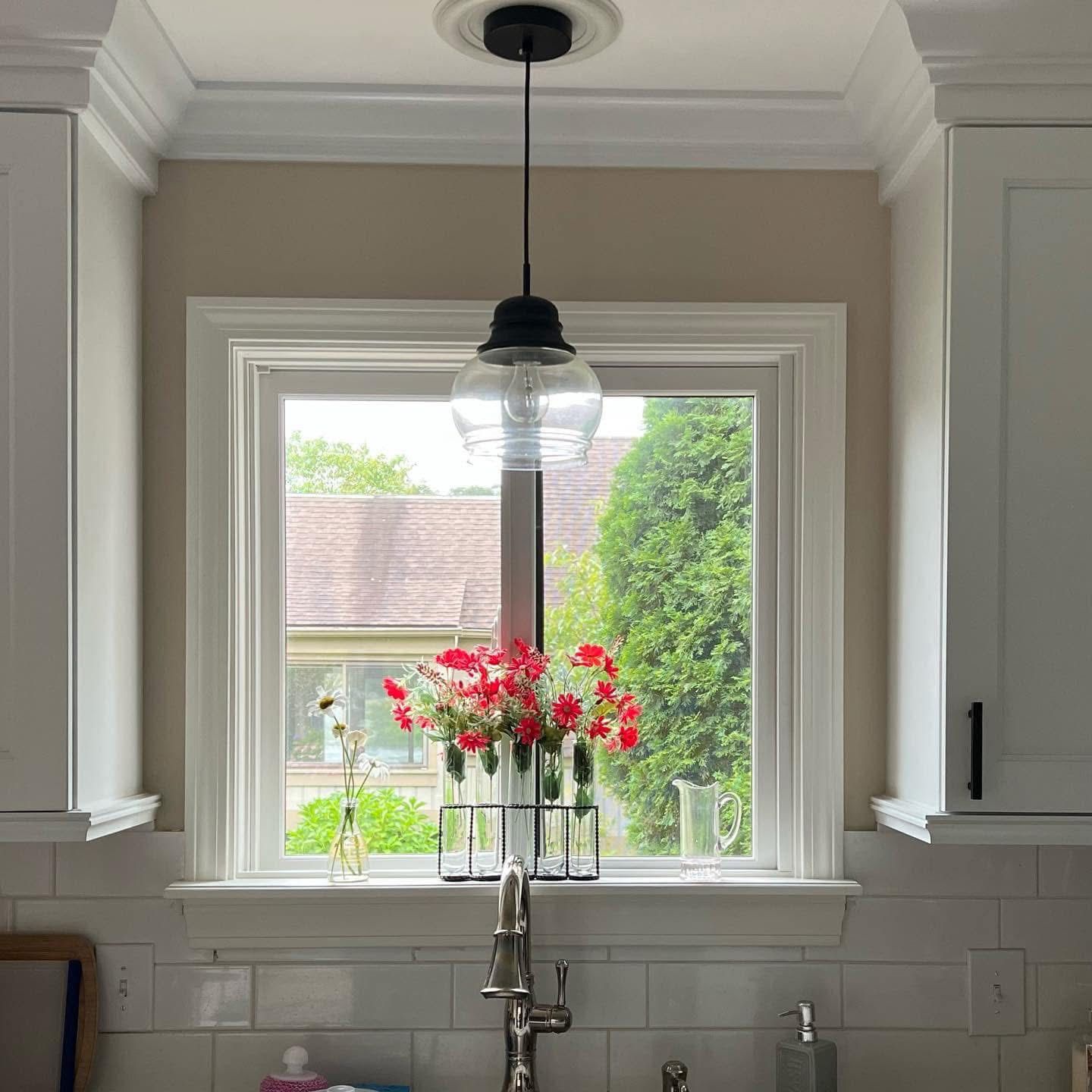 Kitchen window with black pendant light, white cabinets, and red flowers.