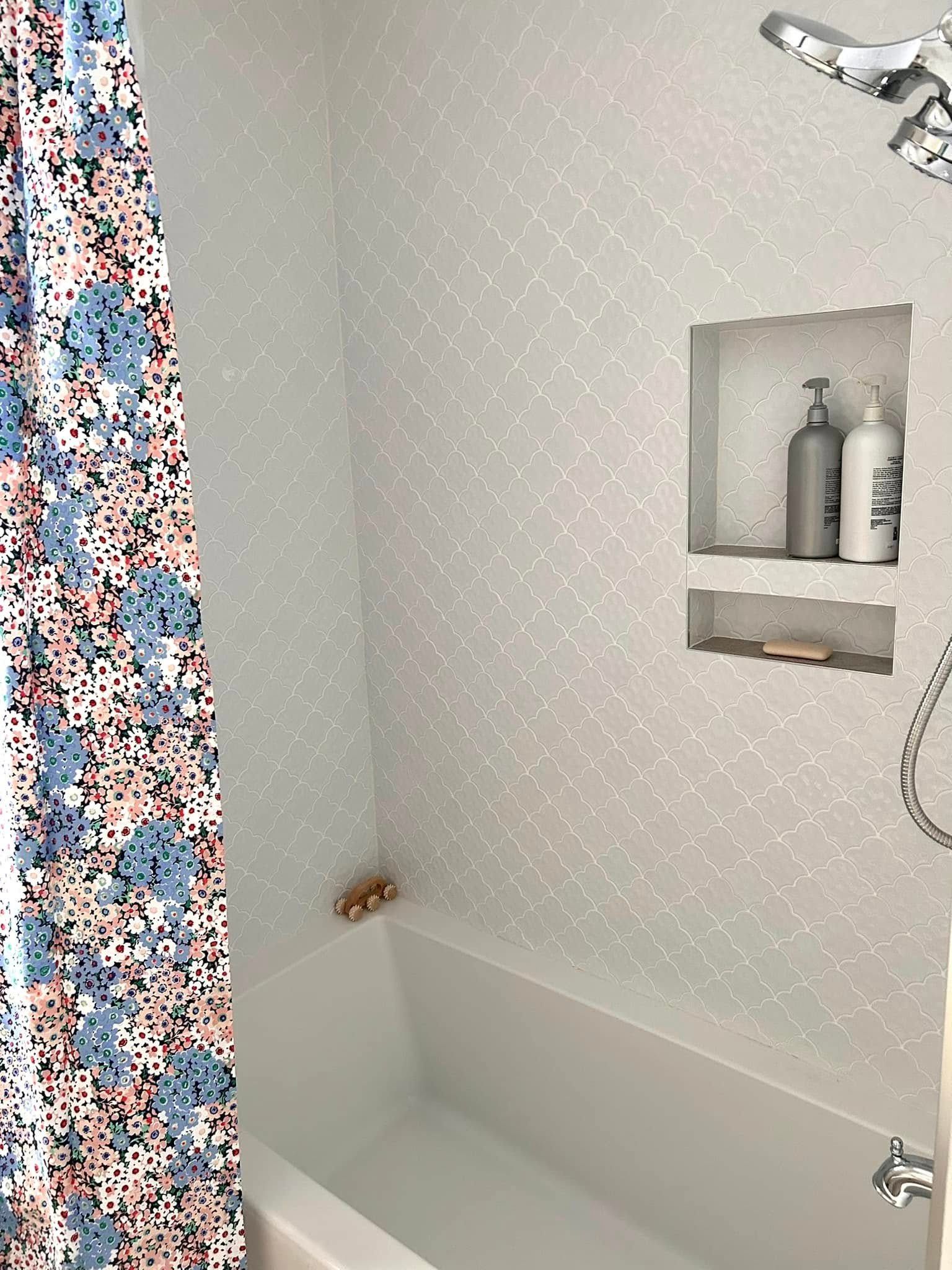 Bathroom with white tile walls and a built-in shelf. A floral shower curtain is visible on the left.