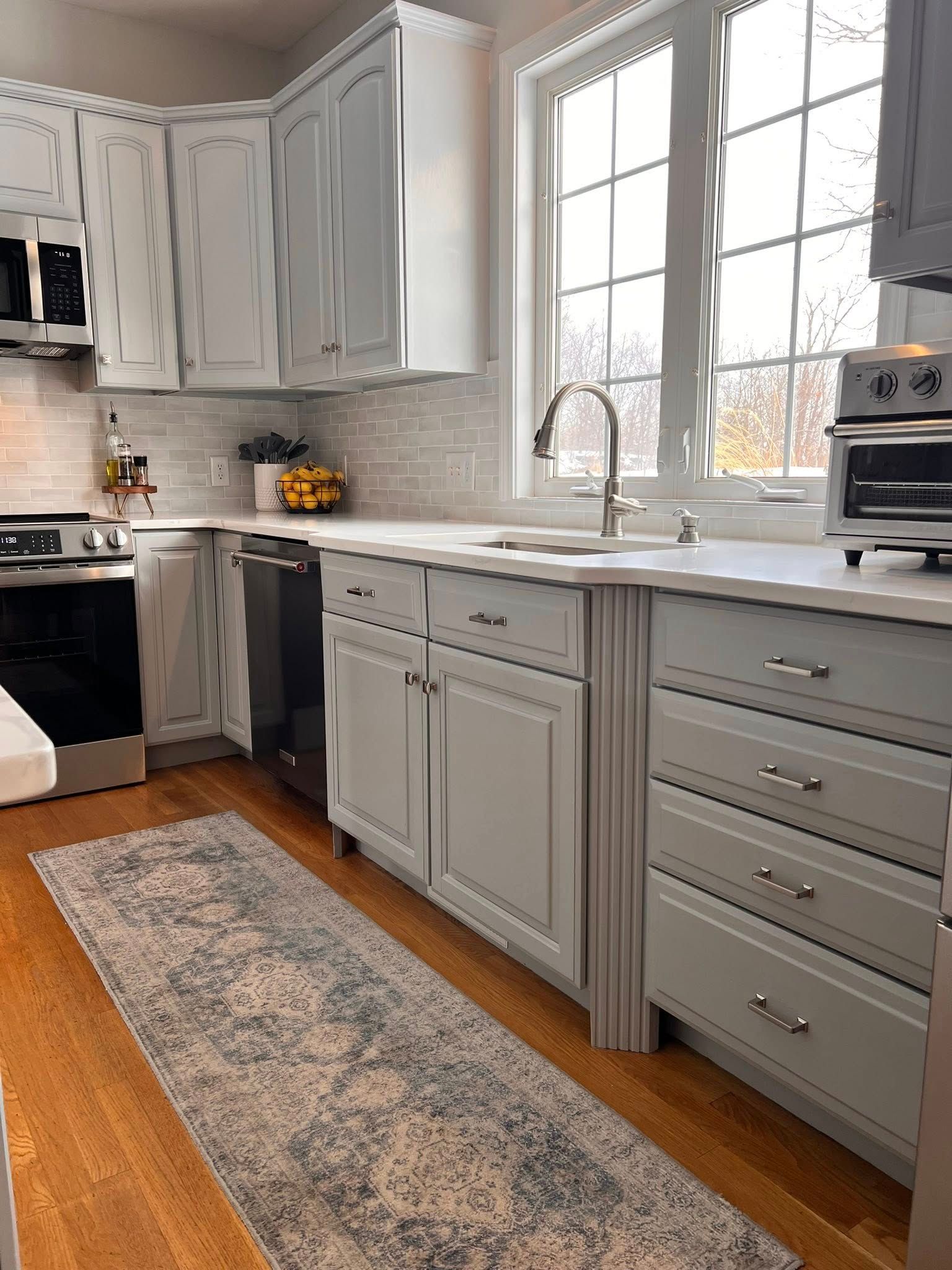 Gray and white kitchen with cabinets, sink, and a patterned runner rug on hardwood flooring.