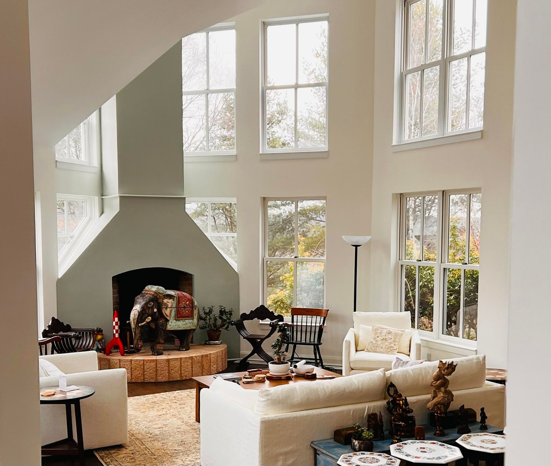 Living room with high ceilings, fireplace, large windows, and white couches.