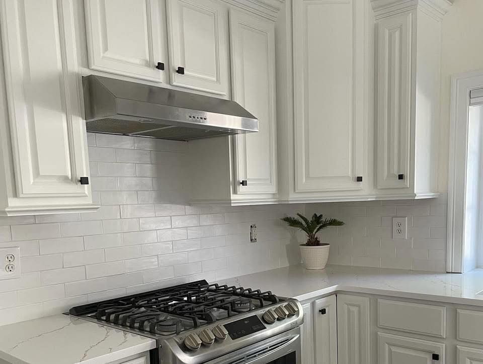 White kitchen with stainless steel range hood, stove, and cabinets.