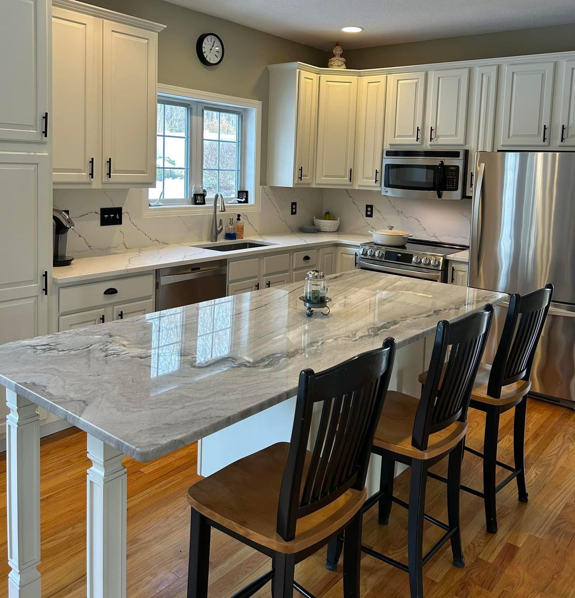 Kitchen with white cabinets, marble countertops, stainless steel appliances, and wooden bar stools.