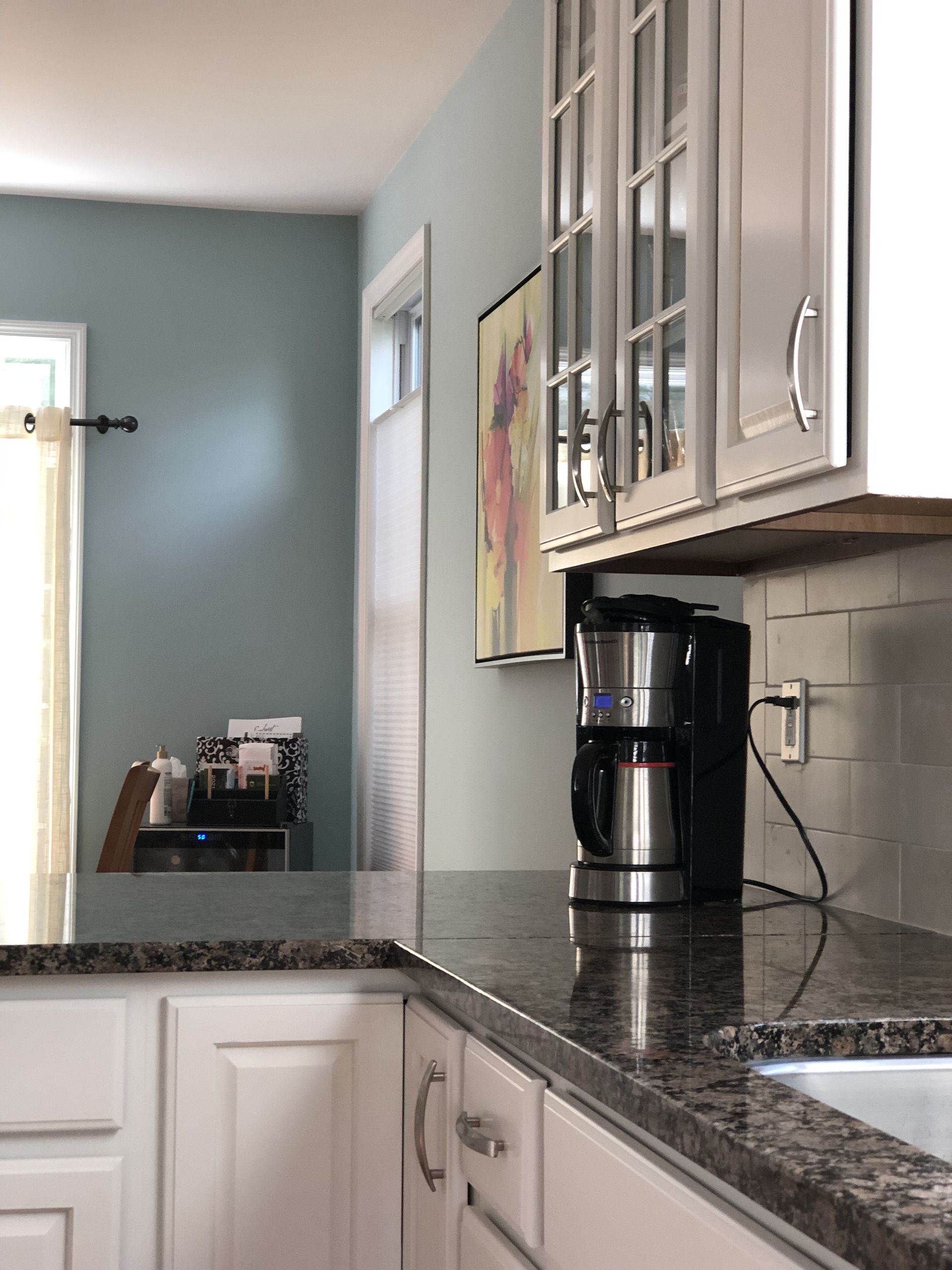 Kitchen corner with white cabinets, dark countertop, coffee maker, and blue wall.