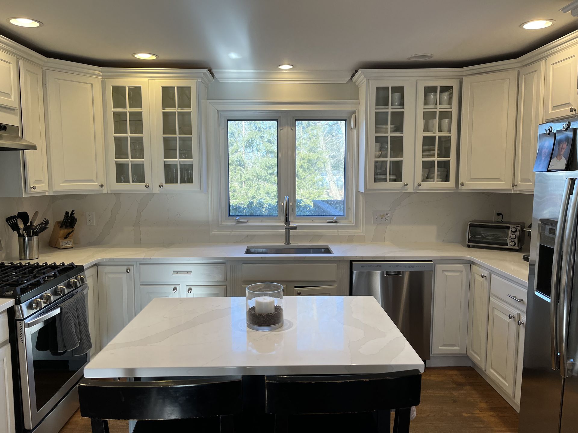White kitchen with cabinets, island, stainless steel appliances, and a window.