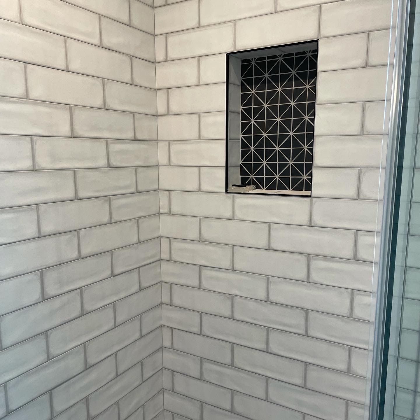 White tiled shower with a patterned tile niche.