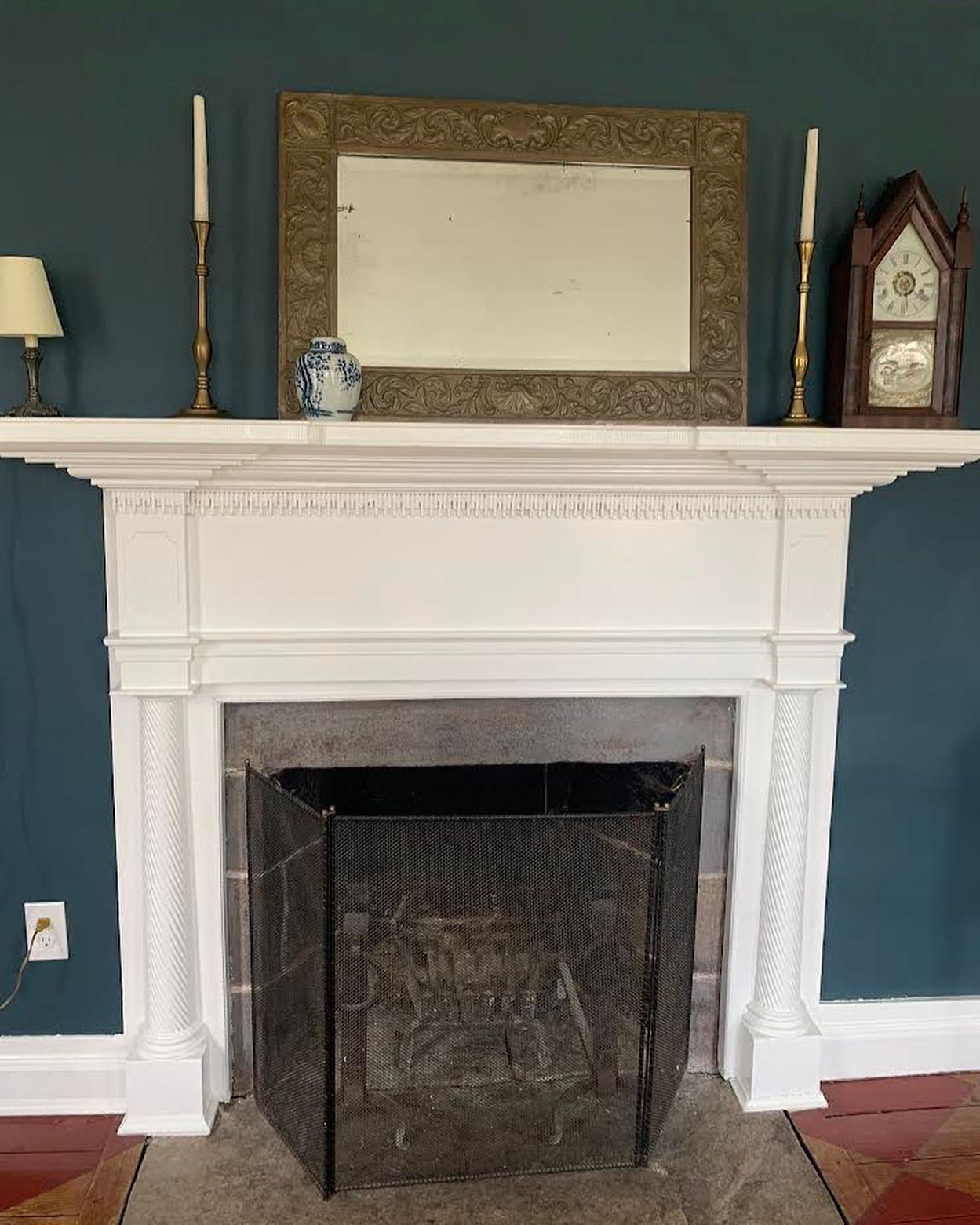 White fireplace with mirror and decor against teal wall.