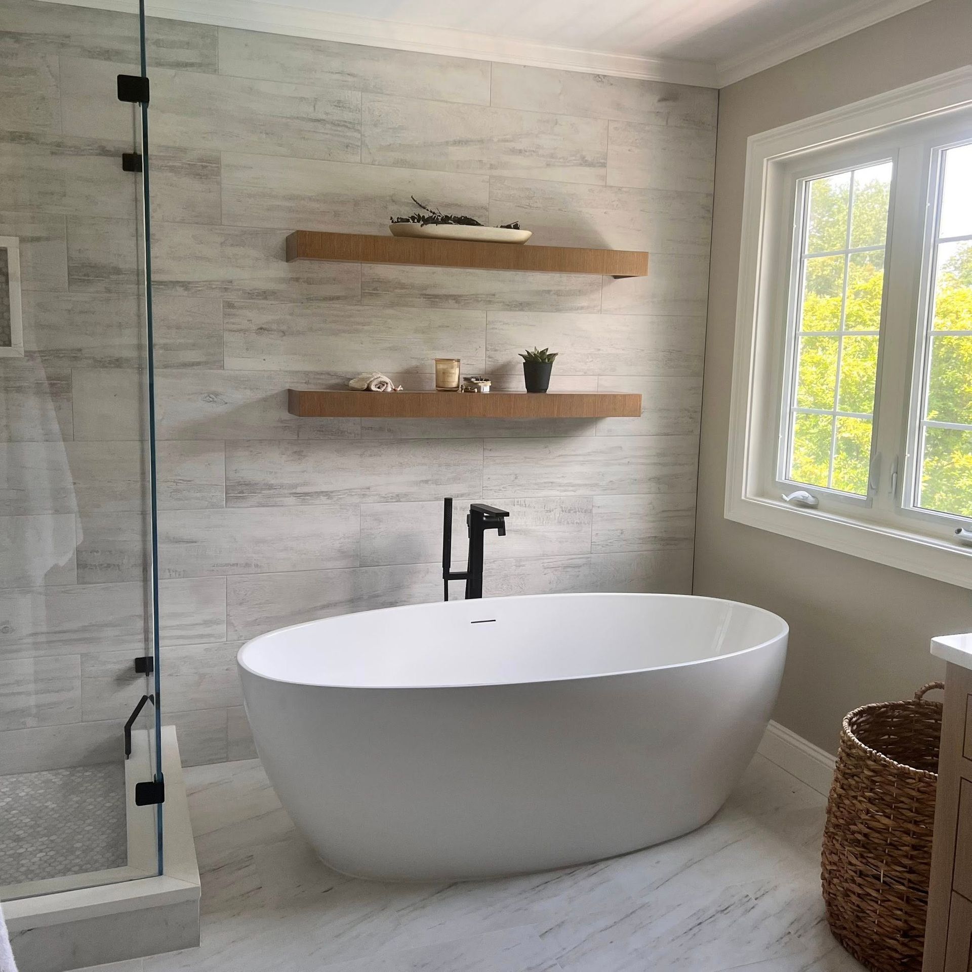 Bathroom with white soaking tub, wood shelves, and large window.