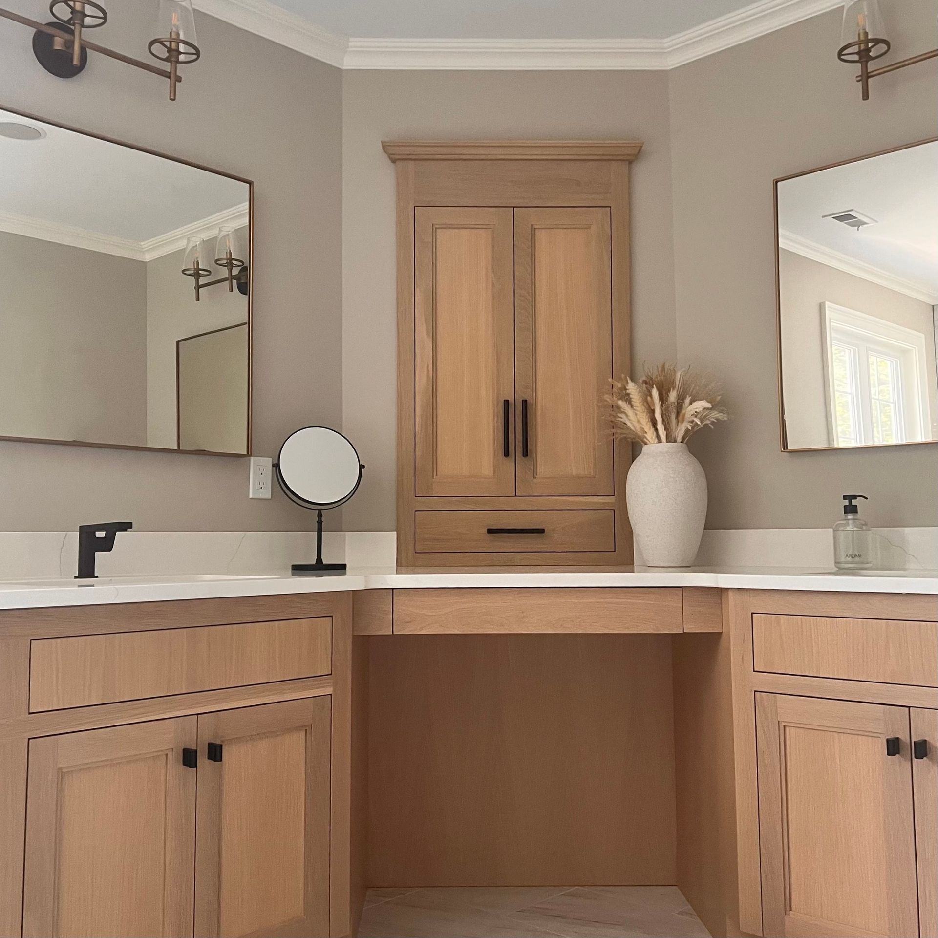 Bathroom with light wood cabinets, white countertops, mirrors, and a central cabinet.