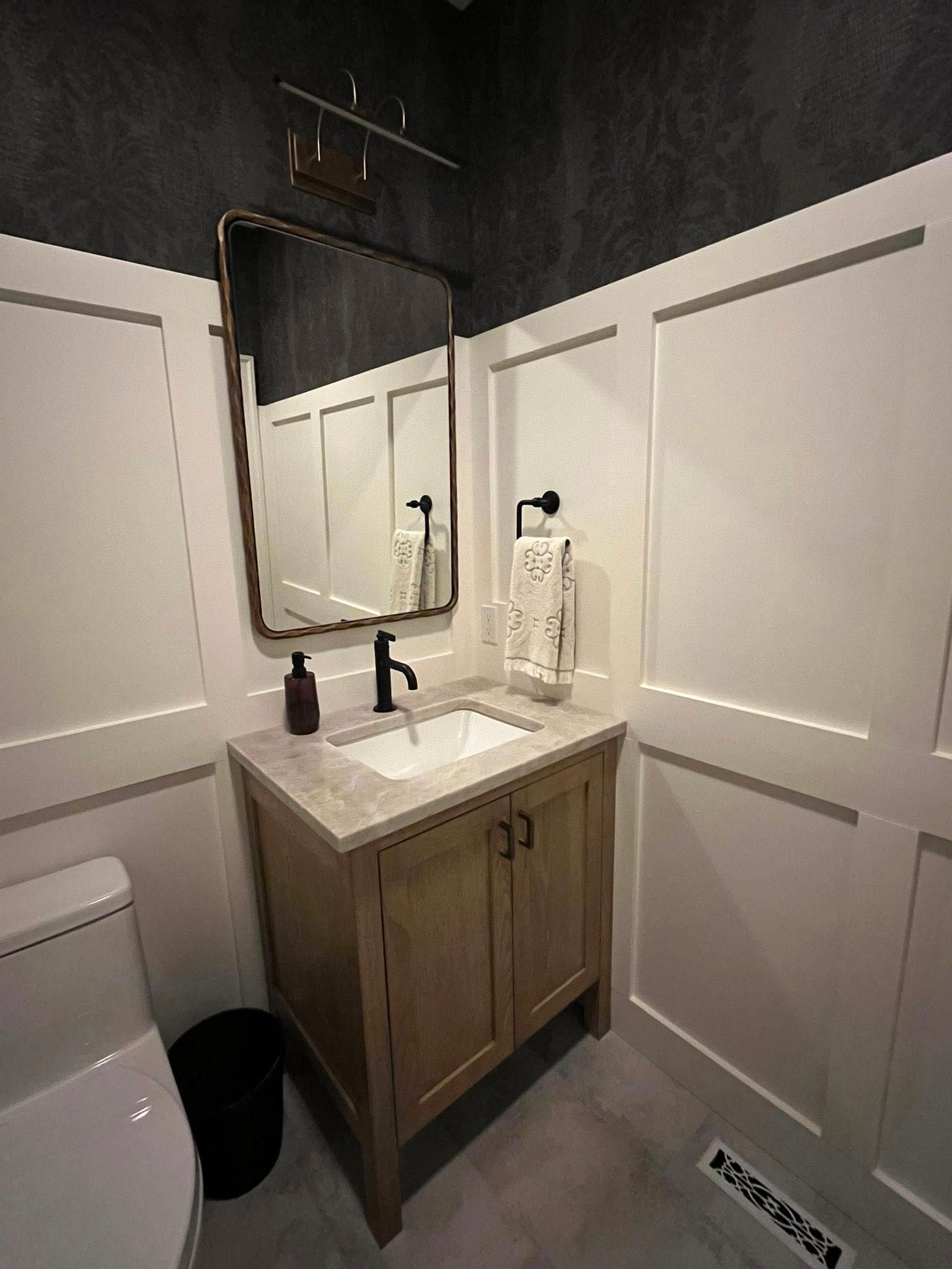 Small powder room with a wood vanity, black fixtures, and a large mirror.