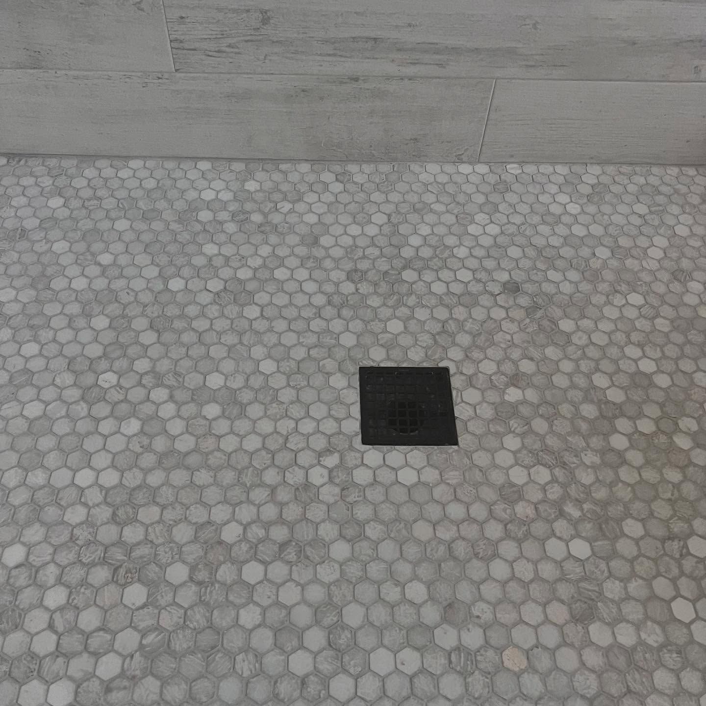 Shower floor with hexagonal gray and white tiles, black square drain, and light gray wall.