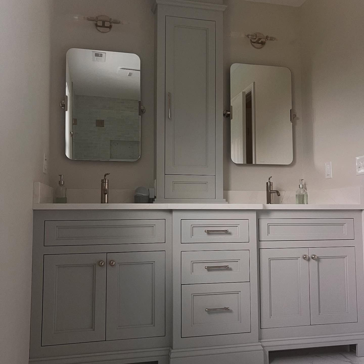 Bathroom with gray cabinets, white countertop, two mirrors, and a tall cabinet.