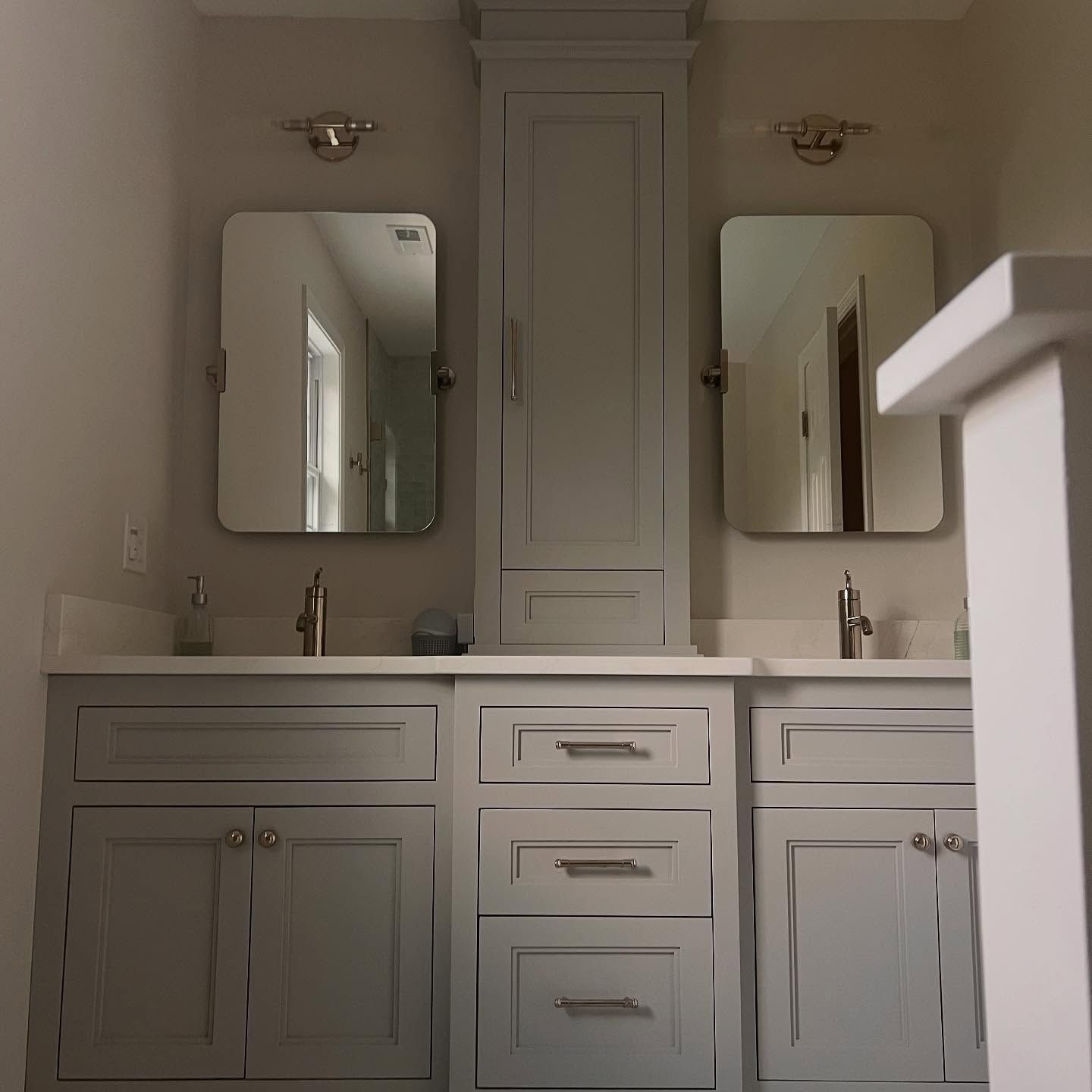 Bathroom with two sinks, gray cabinets, mirrors, and a tall cabinet in between.