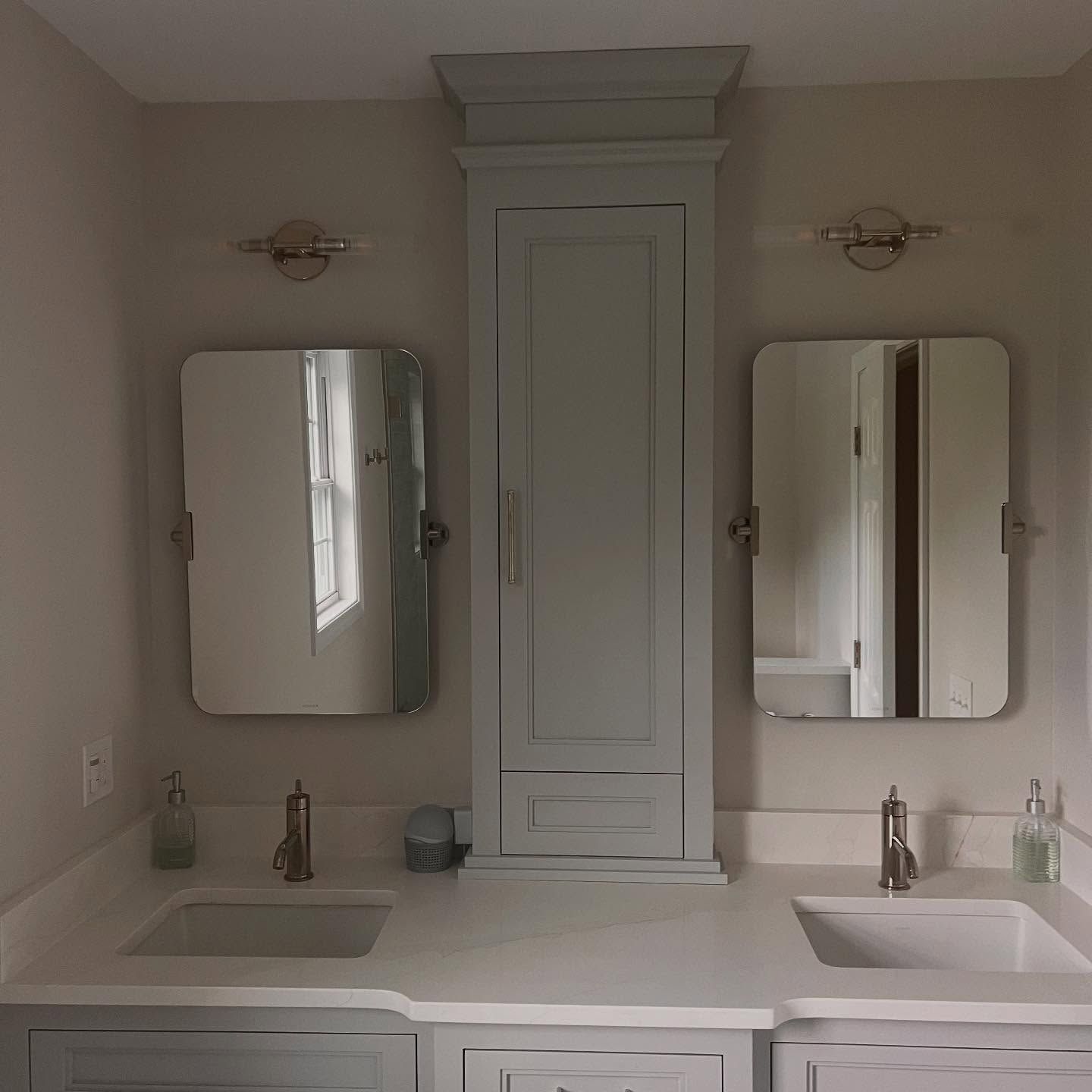 Bathroom with light gray vanity, dual sinks, mirrors, and a central cabinet.