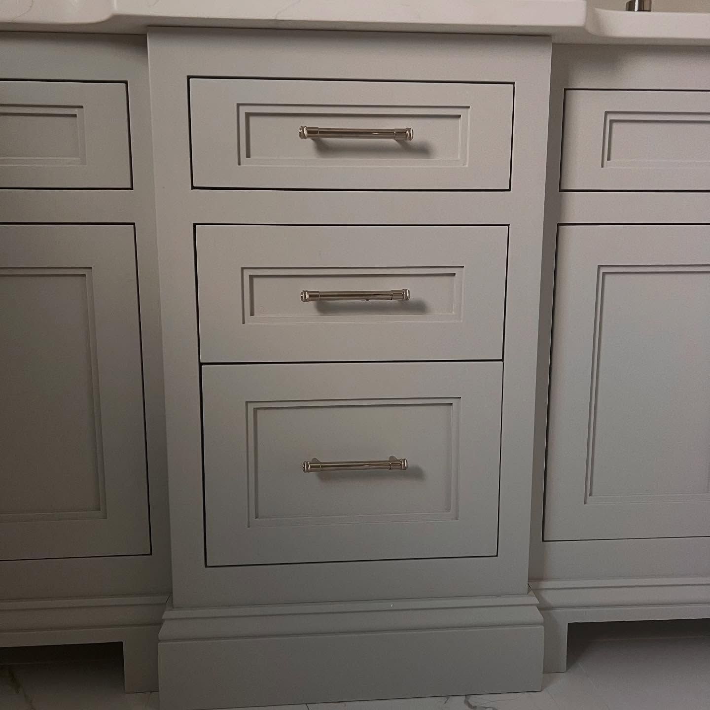 Gray bathroom vanity with three drawers and silver handles.