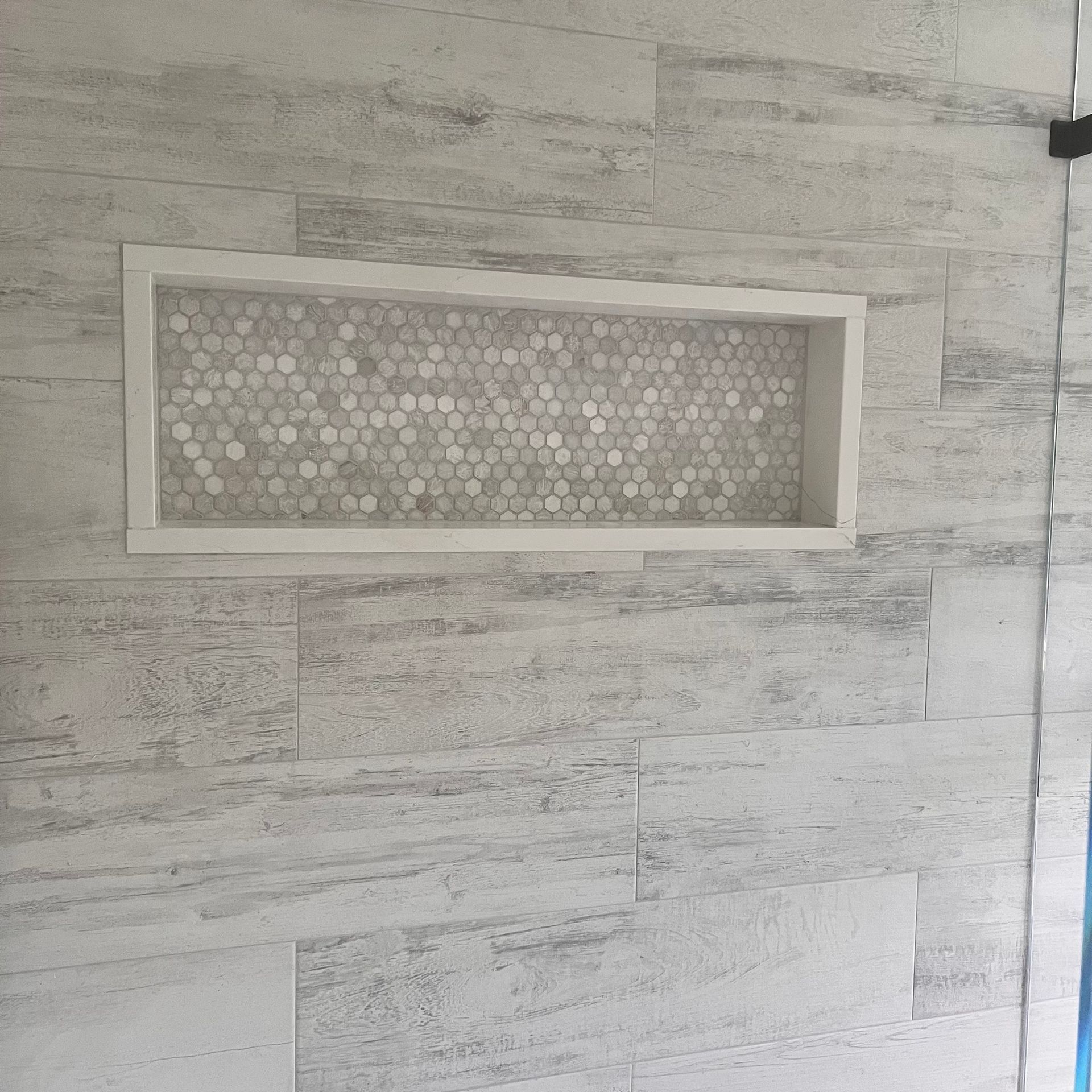 Shower wall with rectangular shelf. White and gray tiled wall with a mosaic shelf.