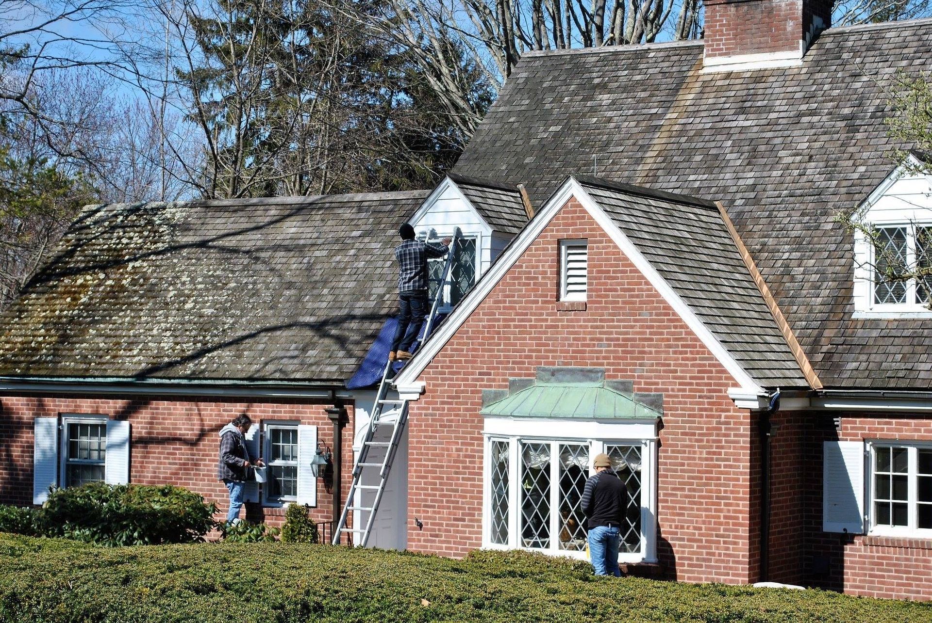 Two men are working on the roof of a brick house.