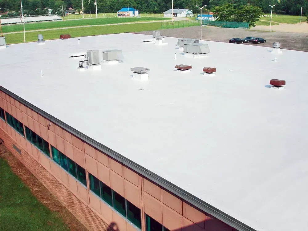 Rooftop of a brick building with vents and HVAC units, bordered by a grassy field and trees beyond.