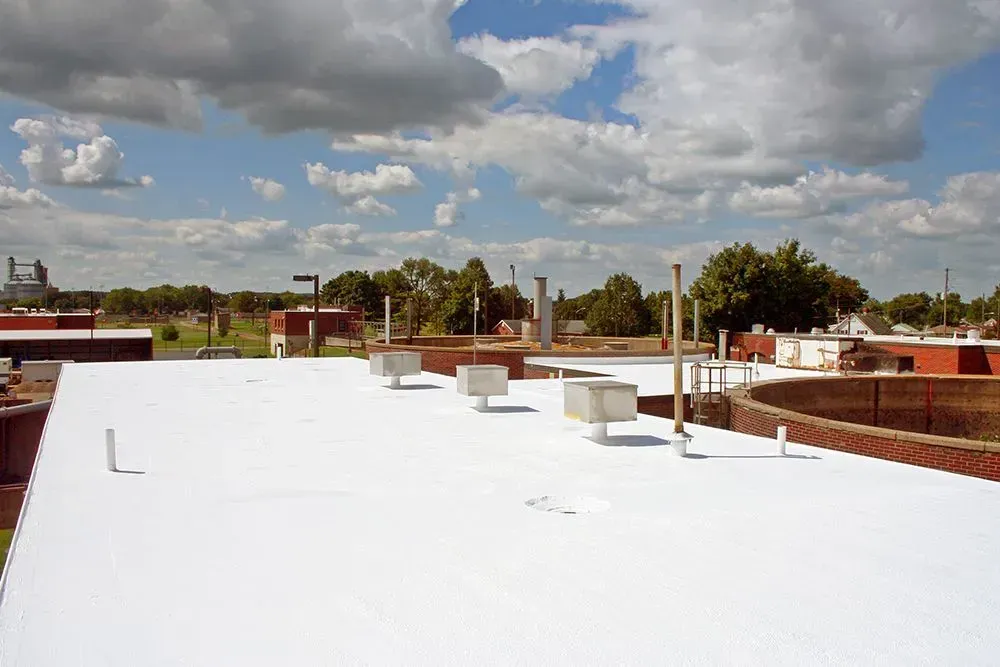 White flat rooftop with vents and pipes under a cloudy sky