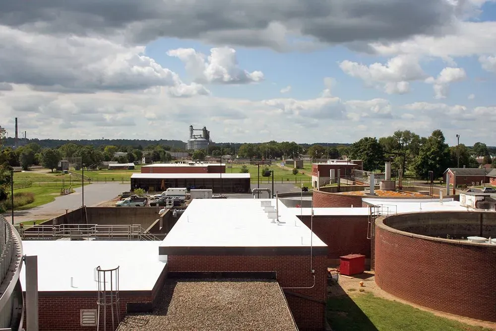 Rooftop view of low brick buildings under a cloudy sky, with trees and a distant water tower.