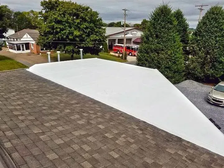Rooftop with dark shingles and a white-coated section, overlooking a suburban street and houses.