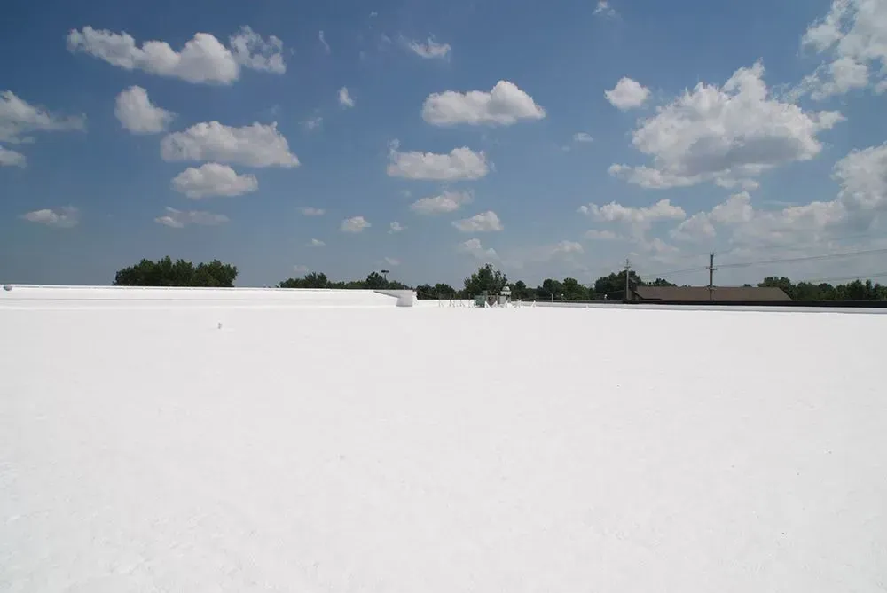 Bright white rooftop under a blue sky with scattered clouds and a distant tree line