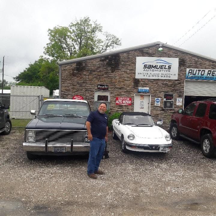 Man standing between a black sedan and white convertible outside an auto repair shop