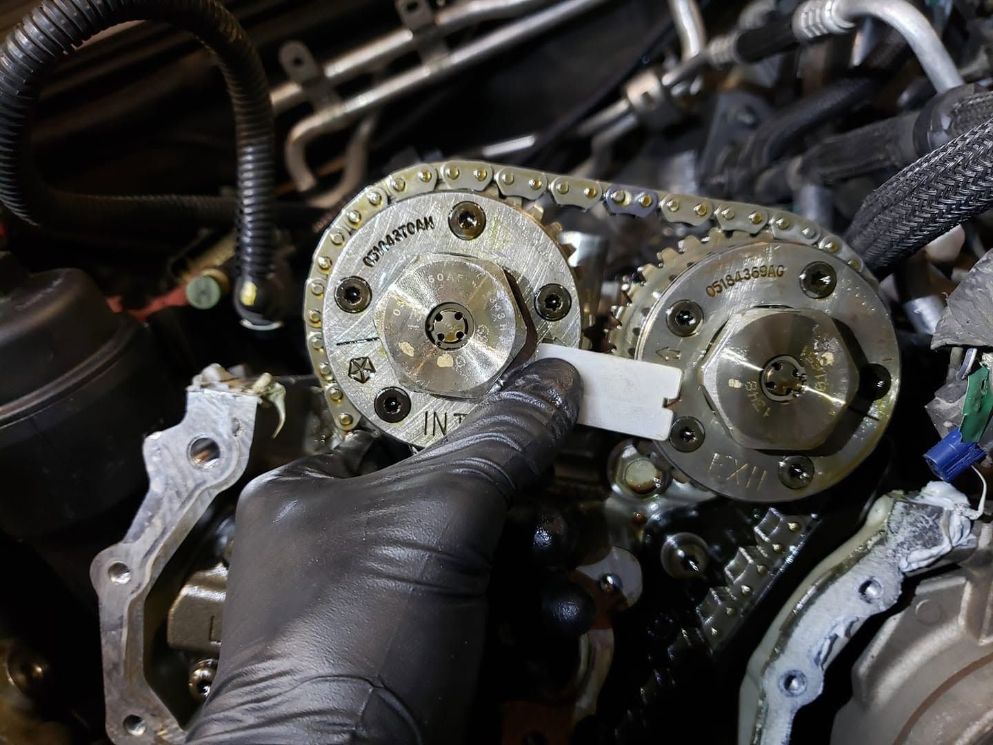 Gloved hands adjusting a car engine timing chain and cam gears close-up