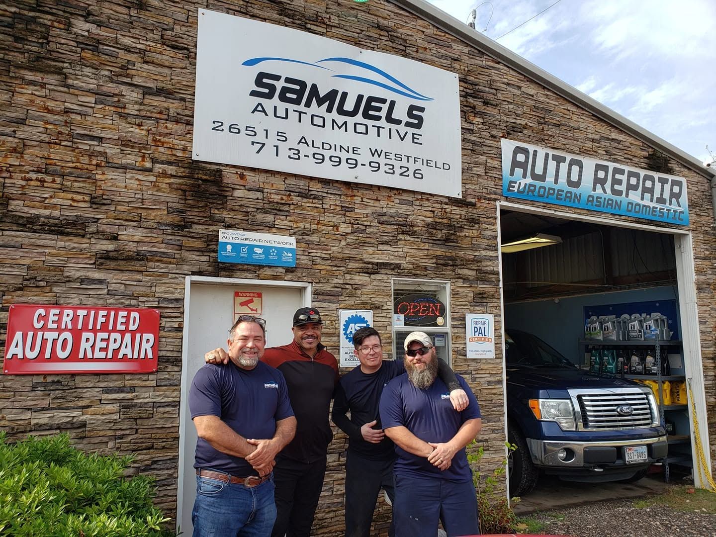 Four people stand outside Samuel’s Automotive and Auto Repair shop beside a parked SUV.