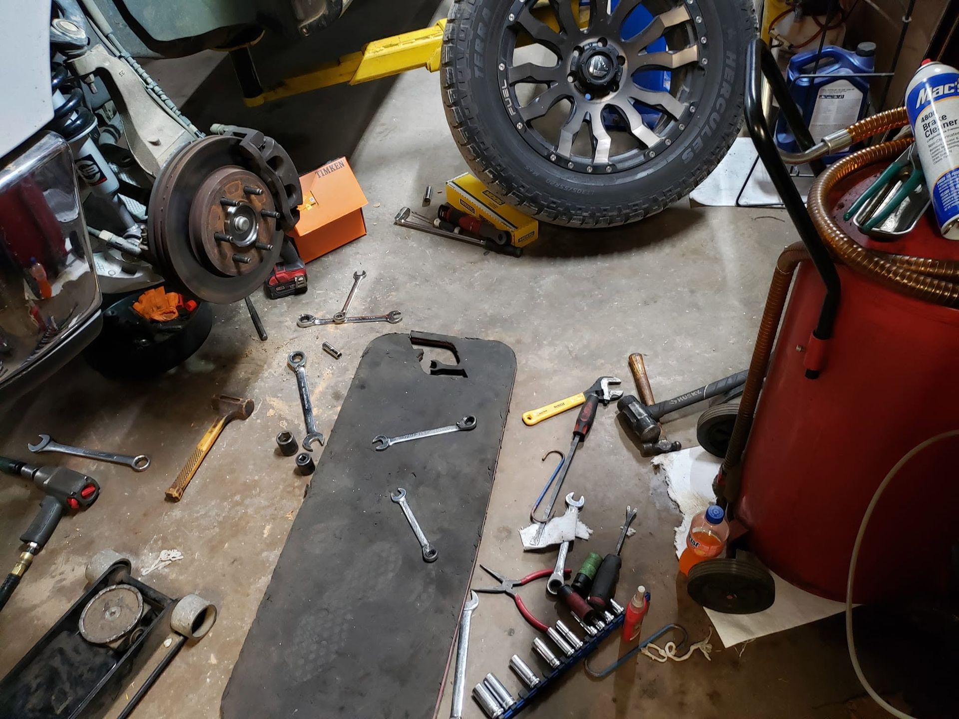 Garage floor with car parts, tools, and a tire near a red tool chest