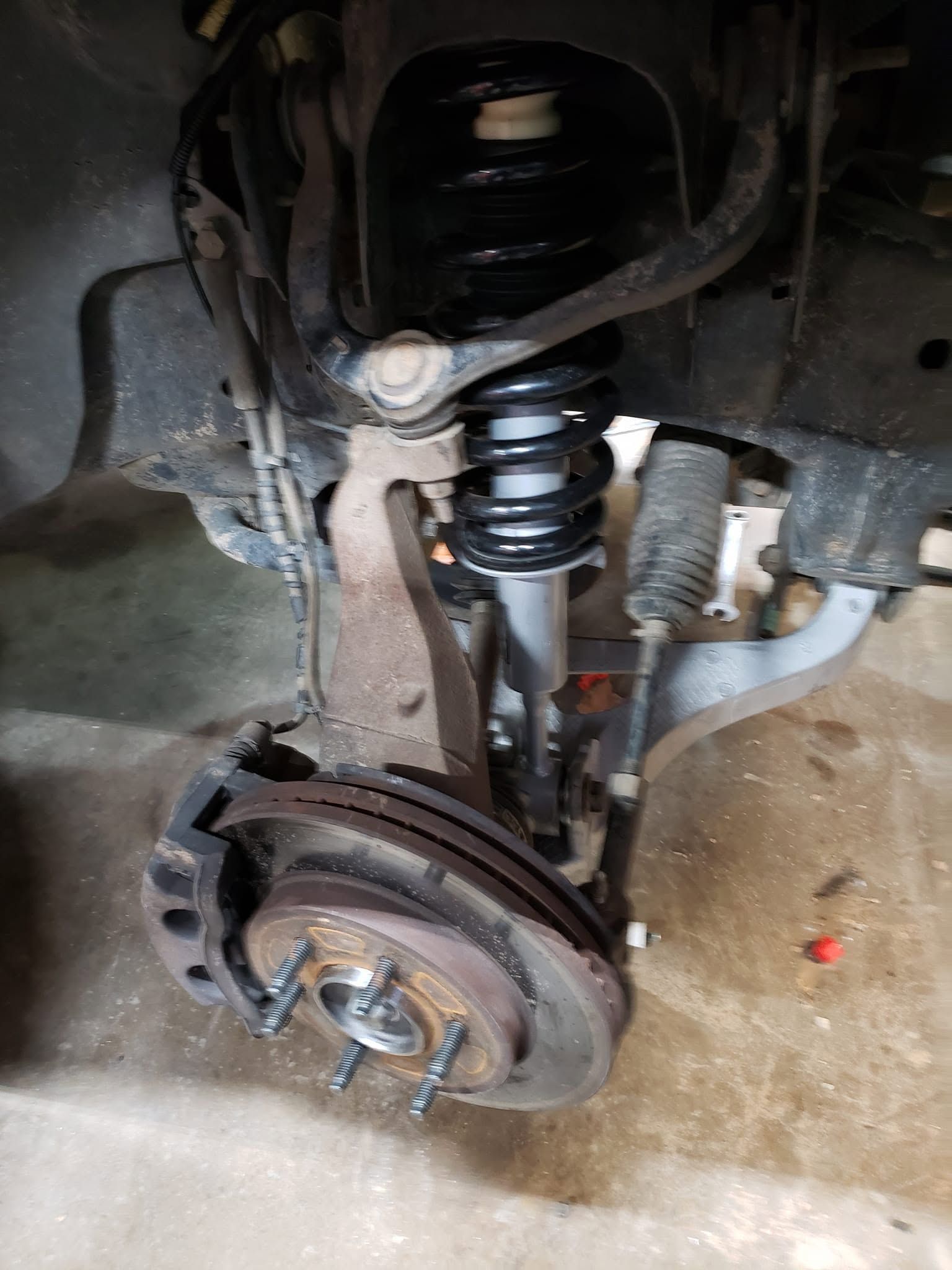 Car wheel removed, showing brake rotor, suspension spring, and wheel well on a vehicle.