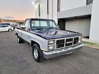 Classic black-and-silver GMC pickup truck parked outdoors near a building at dusk
