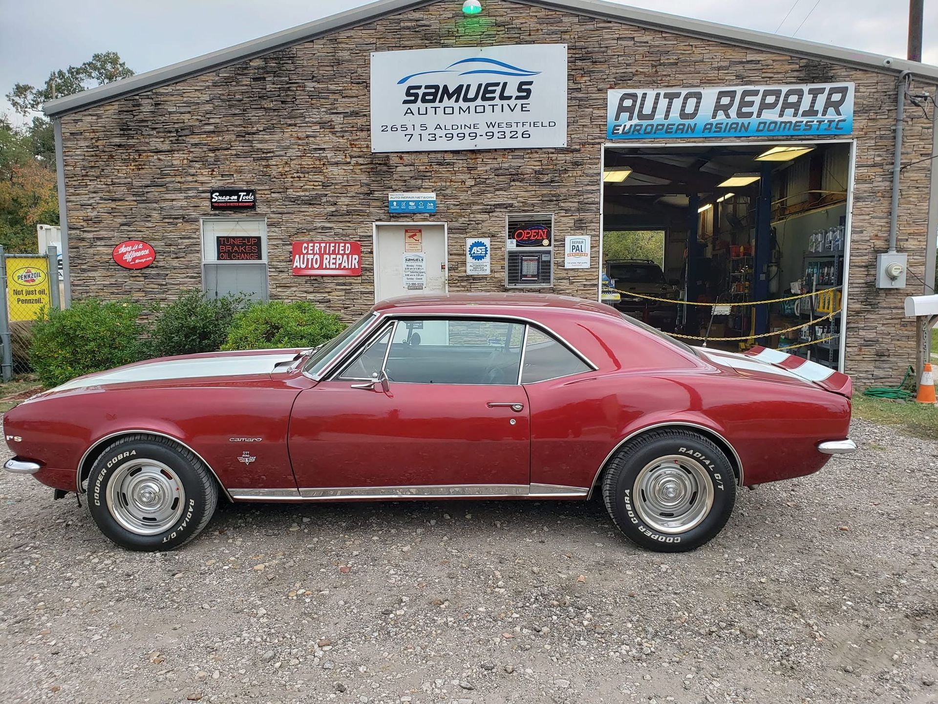 Red classic car parked outside Samuels Auto Repair garage with brick facade