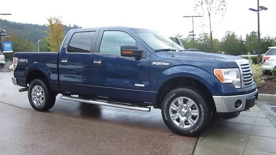 Blue pickup truck parked on a wet dealership lot, side view