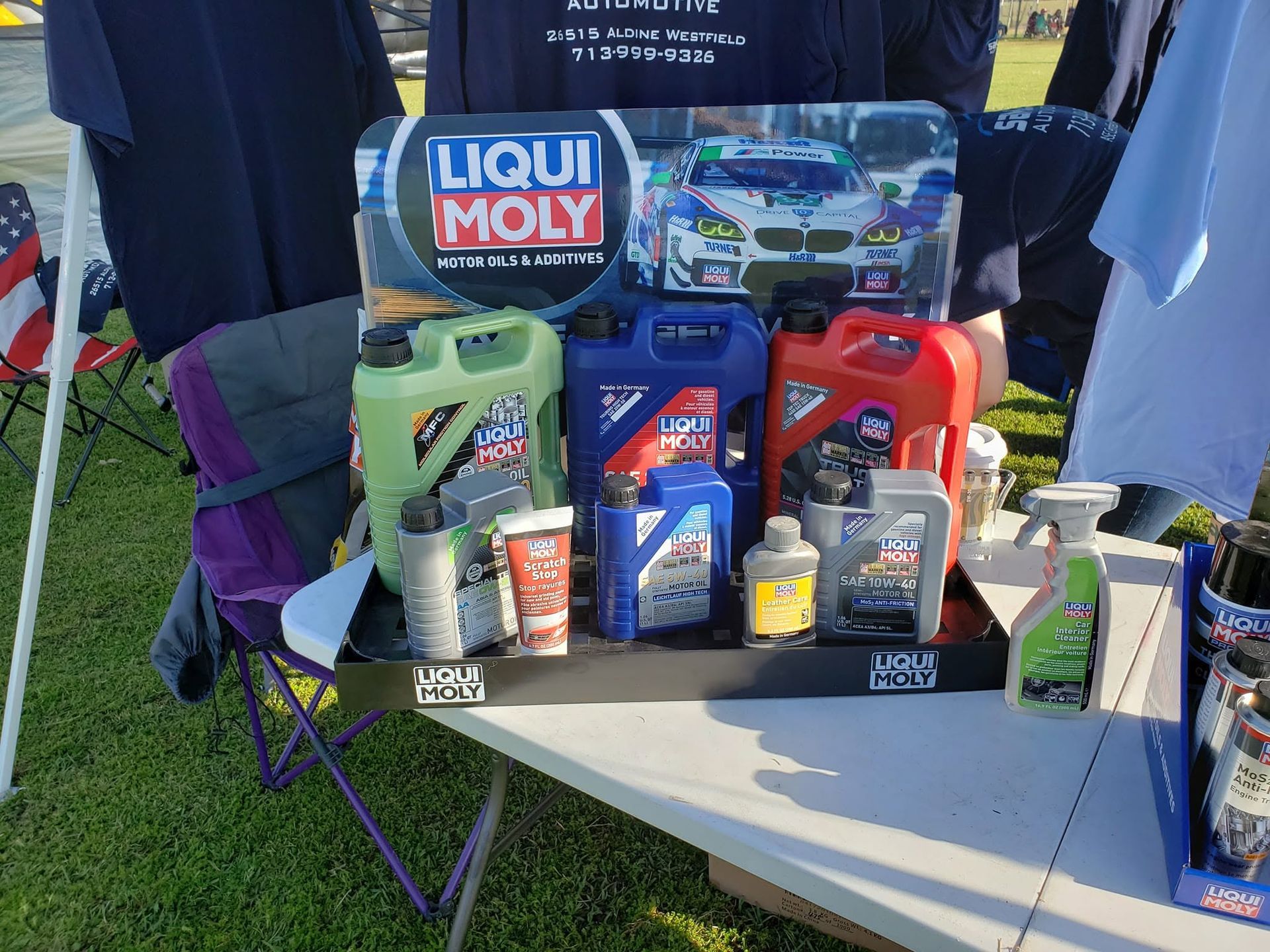 Liqui Moly auto care products displayed on a table at an outdoor booth, with a racing poster backdrop