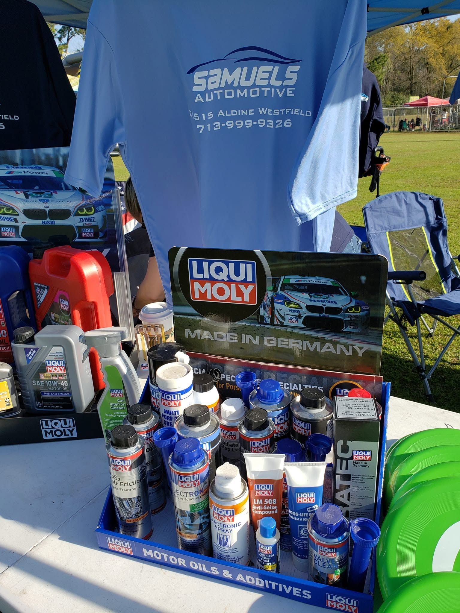 Outdoor display of Liqui Moly products and a blue event shirt on a booth table under a tent.