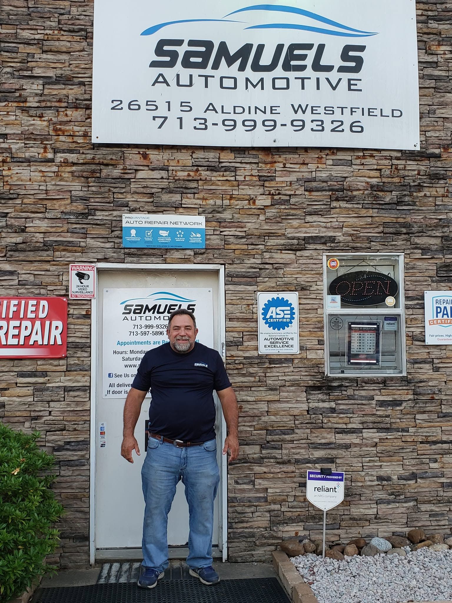 Man standing outside Samuel's Automotive storefront with stone facade and red Certified Repair sign