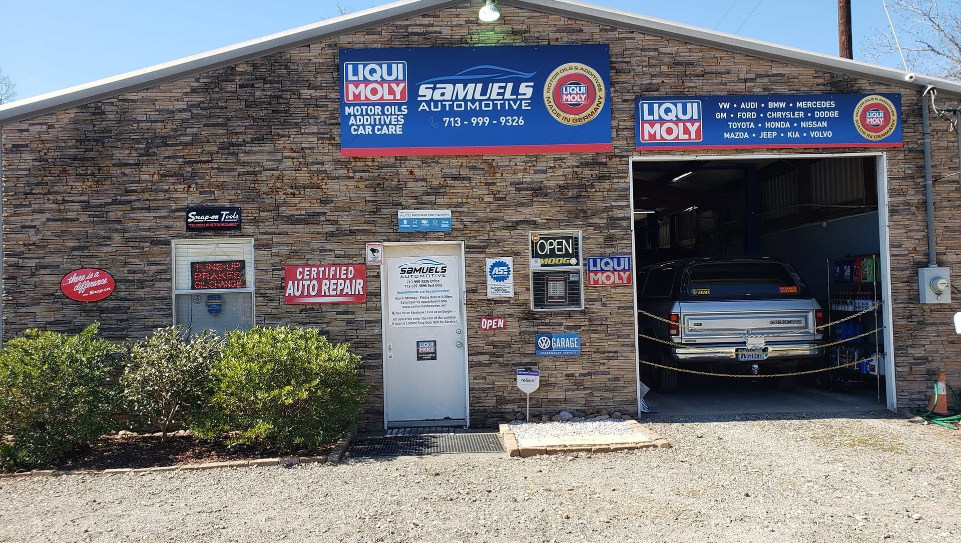 Small brick auto repair shop with blue signage and a car parked inside the open garage bay.