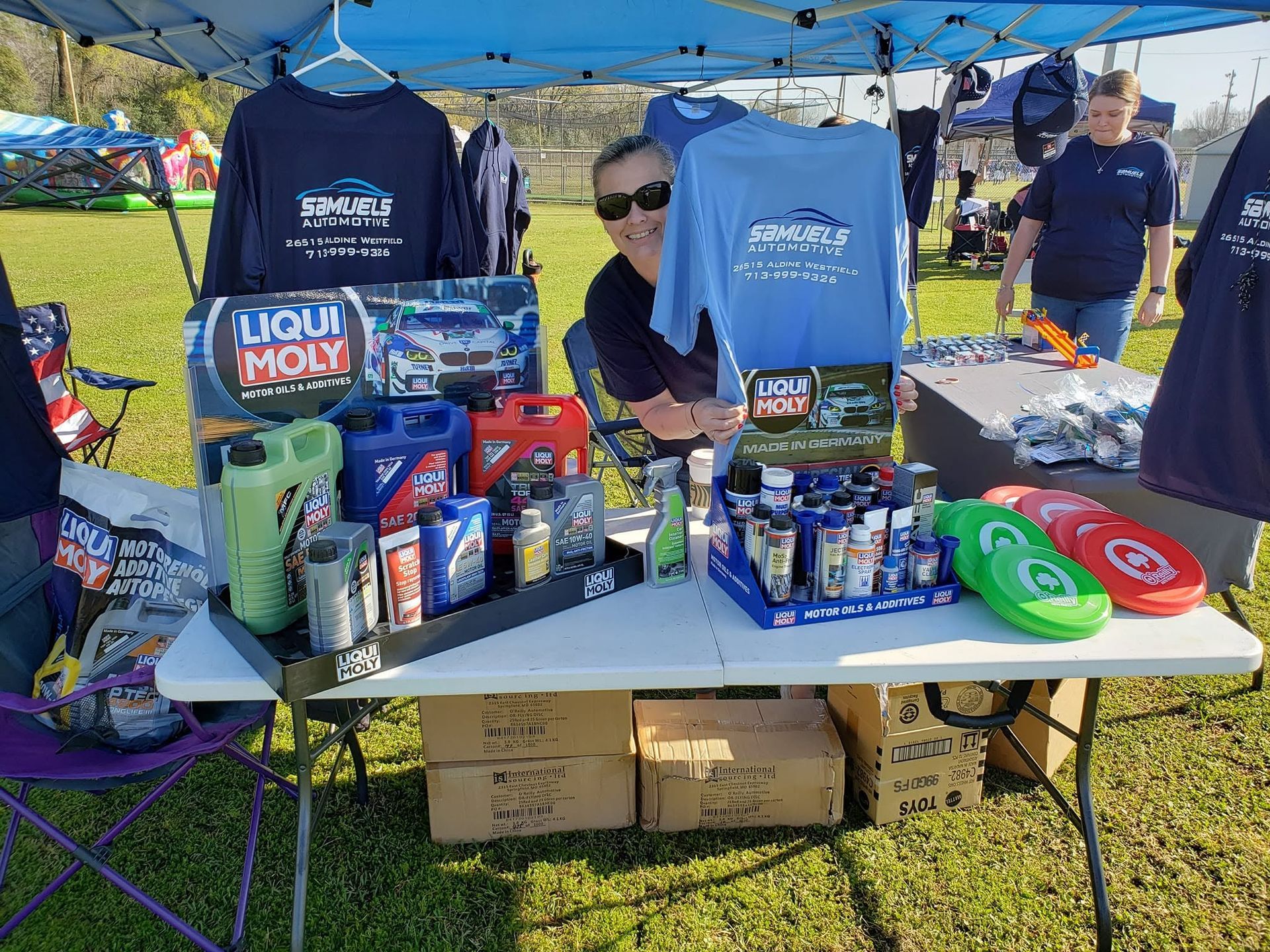 Booth under blue canopy with oil cans and car care products displayed on a table