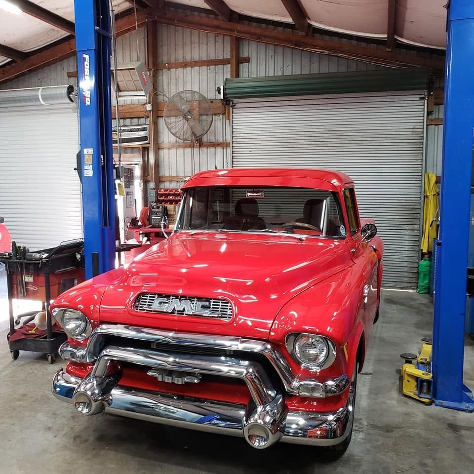 Red classic GMC pickup truck in an auto shop with a lifted hood and blue car lifts