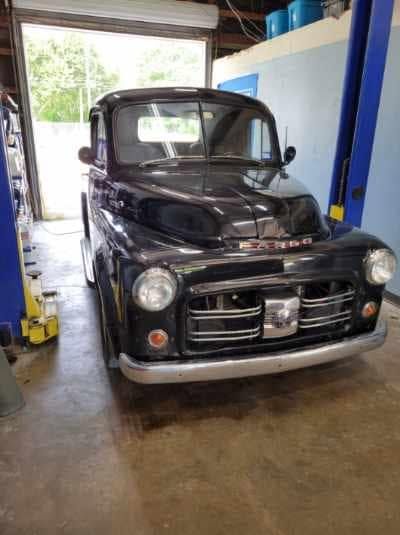 Black vintage pickup truck parked inside a garage with the door open.