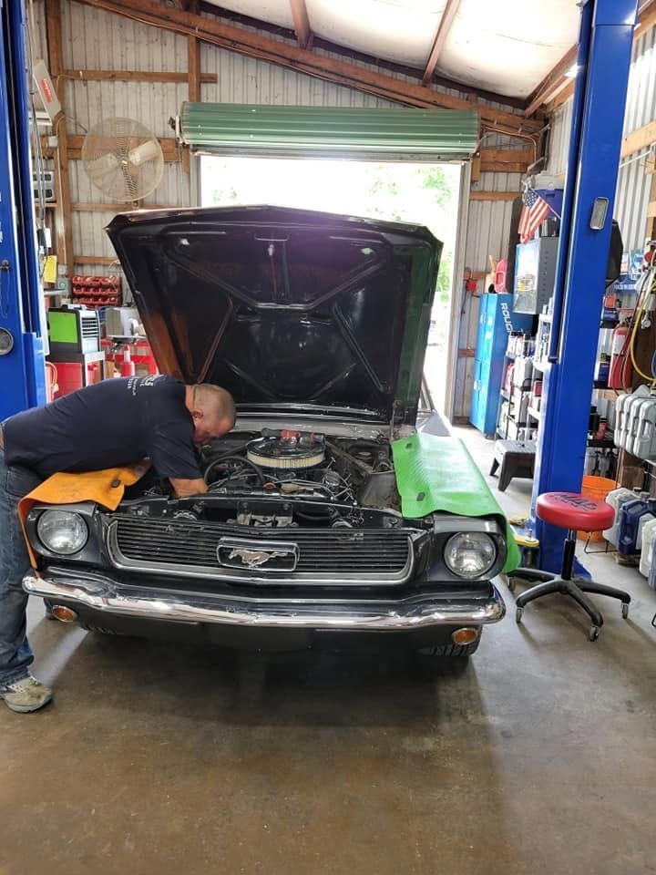 Mechanic inspecting a classic car with its hood open in an auto repair shop