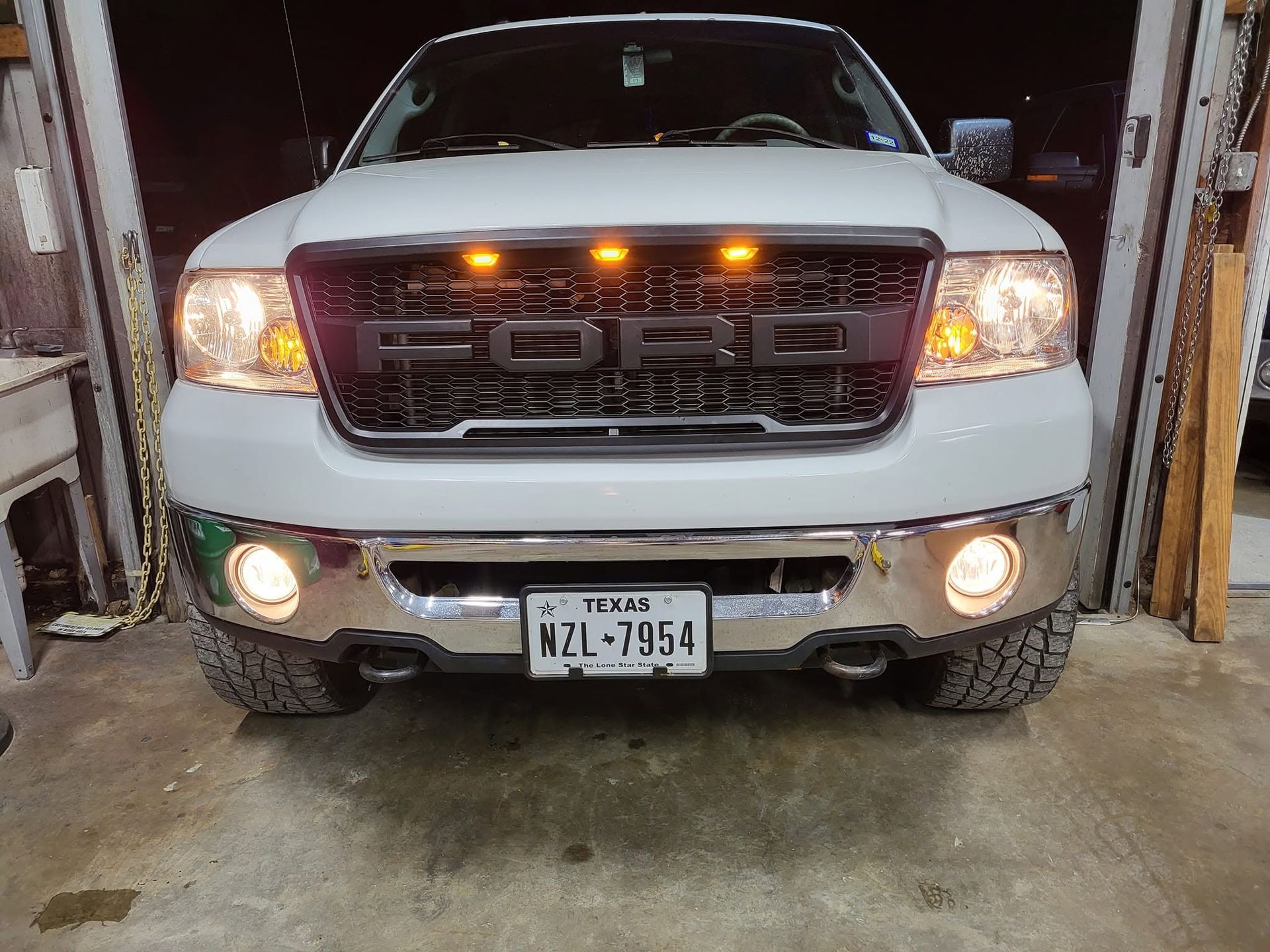 White pickup truck with headlights on inside a garage, viewed from the front.