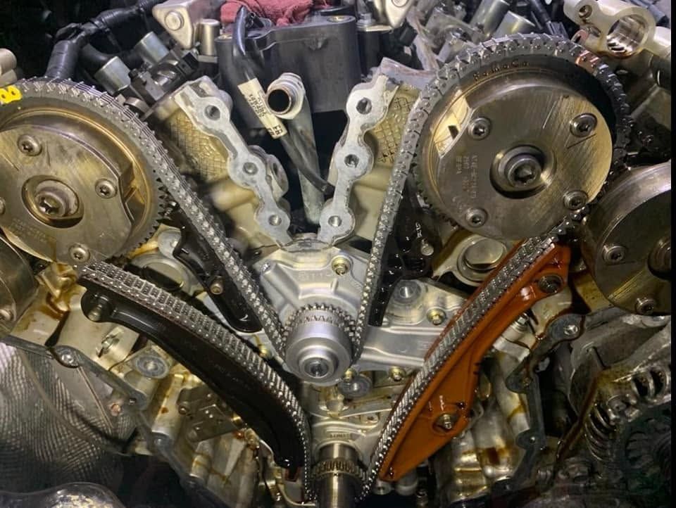 Close-up of an engine timing chain and gears with metal cam sprockets and orange tensioner guides