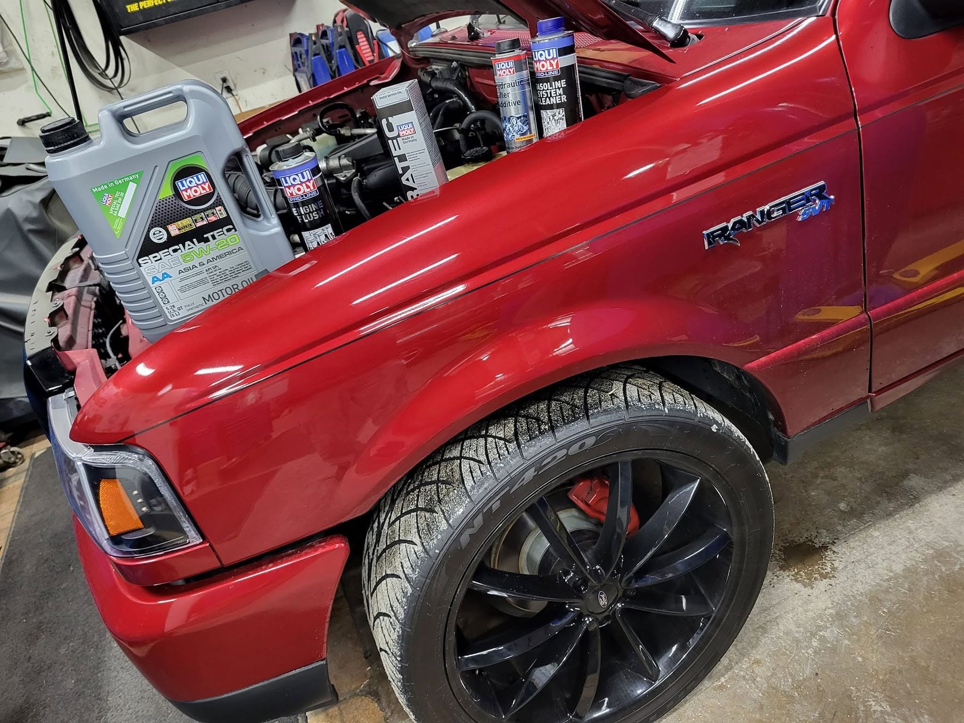 Red pickup truck in a garage, close-up of the front fender and wheel with a lift kit.
