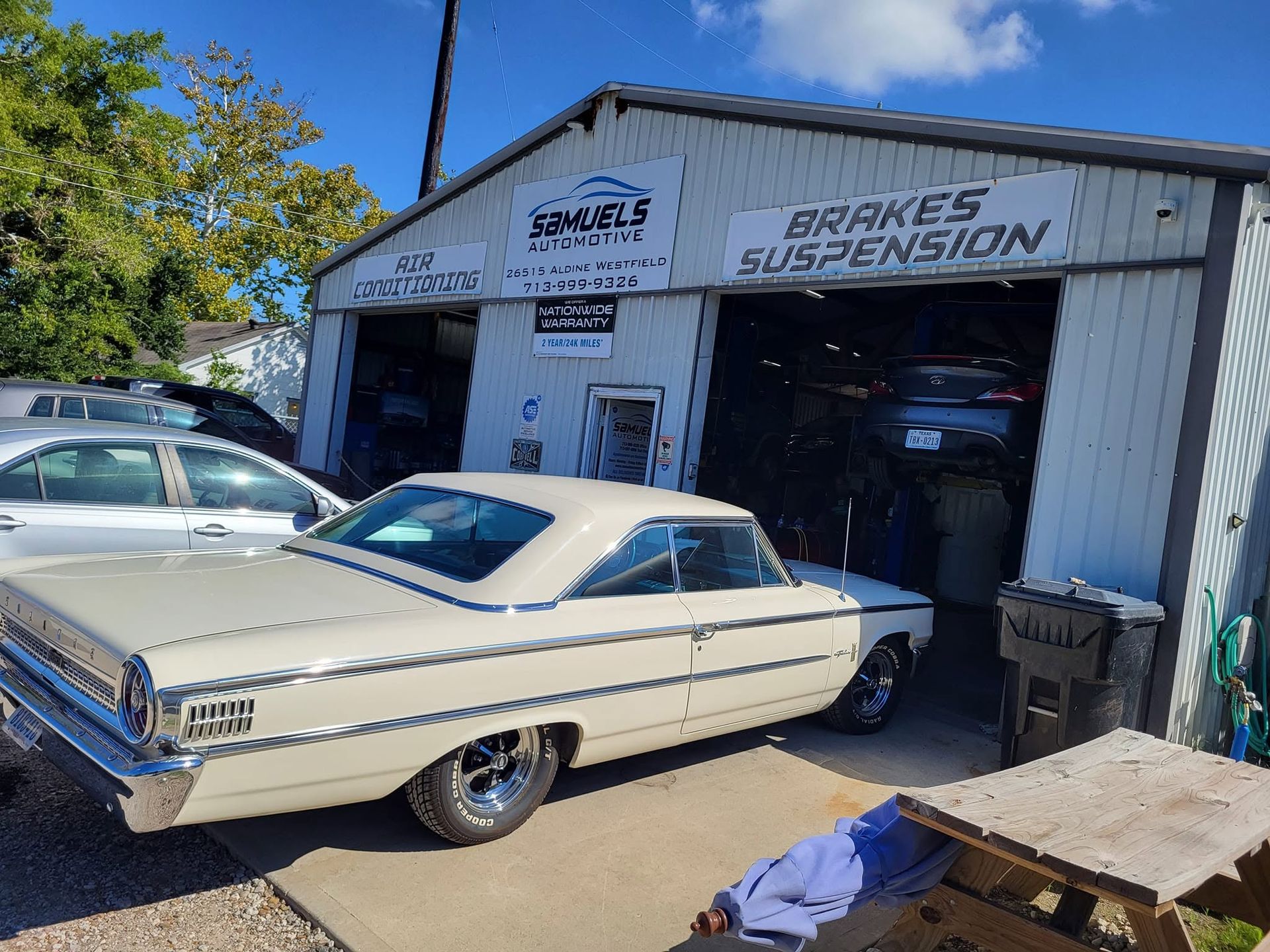 Classic cream coupe parked outside a brake and suspension auto shop under sunny blue skies