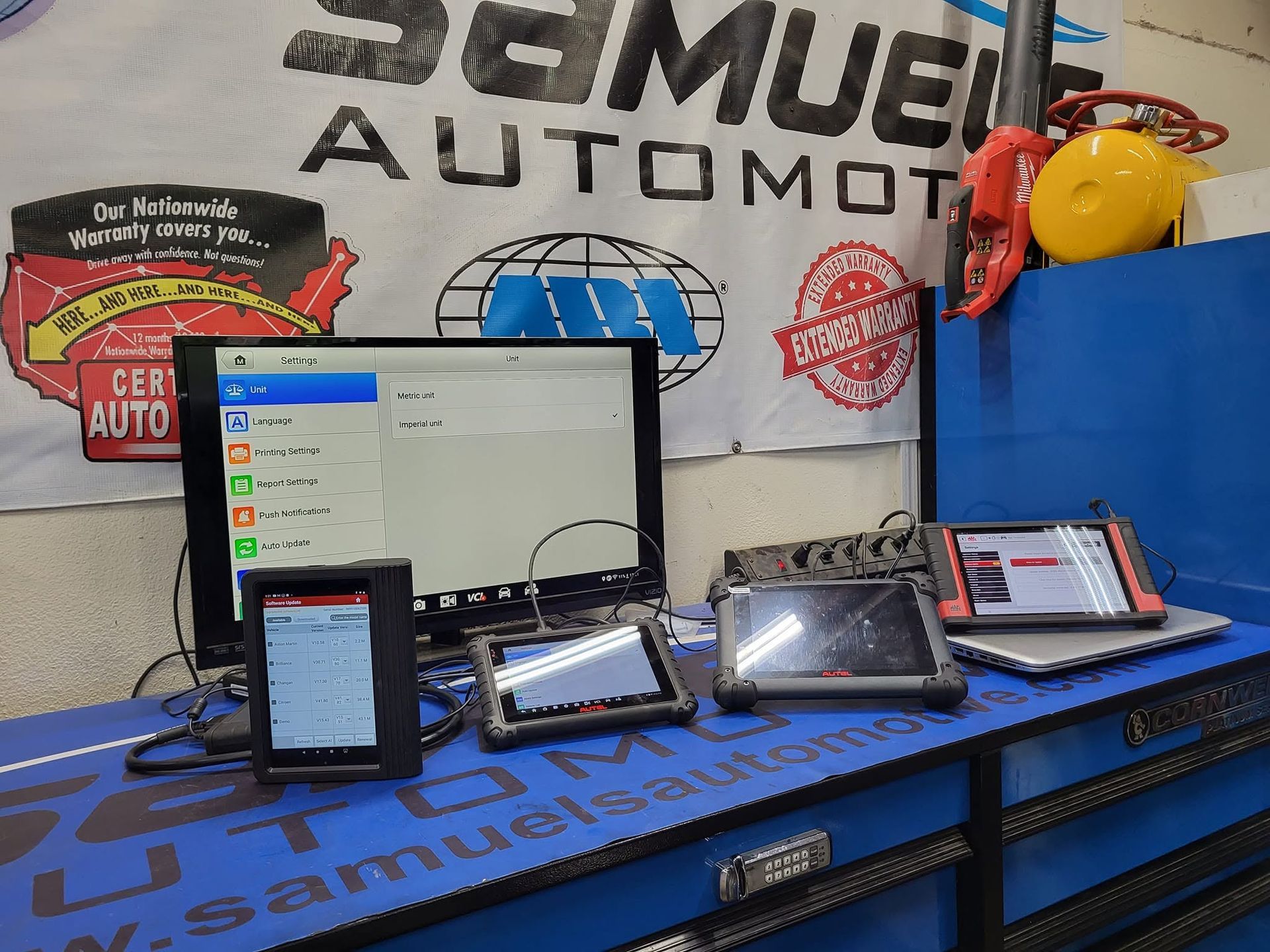 Auto shop workbench with multiple smartphones and a laptop displaying screens on a blue mat.