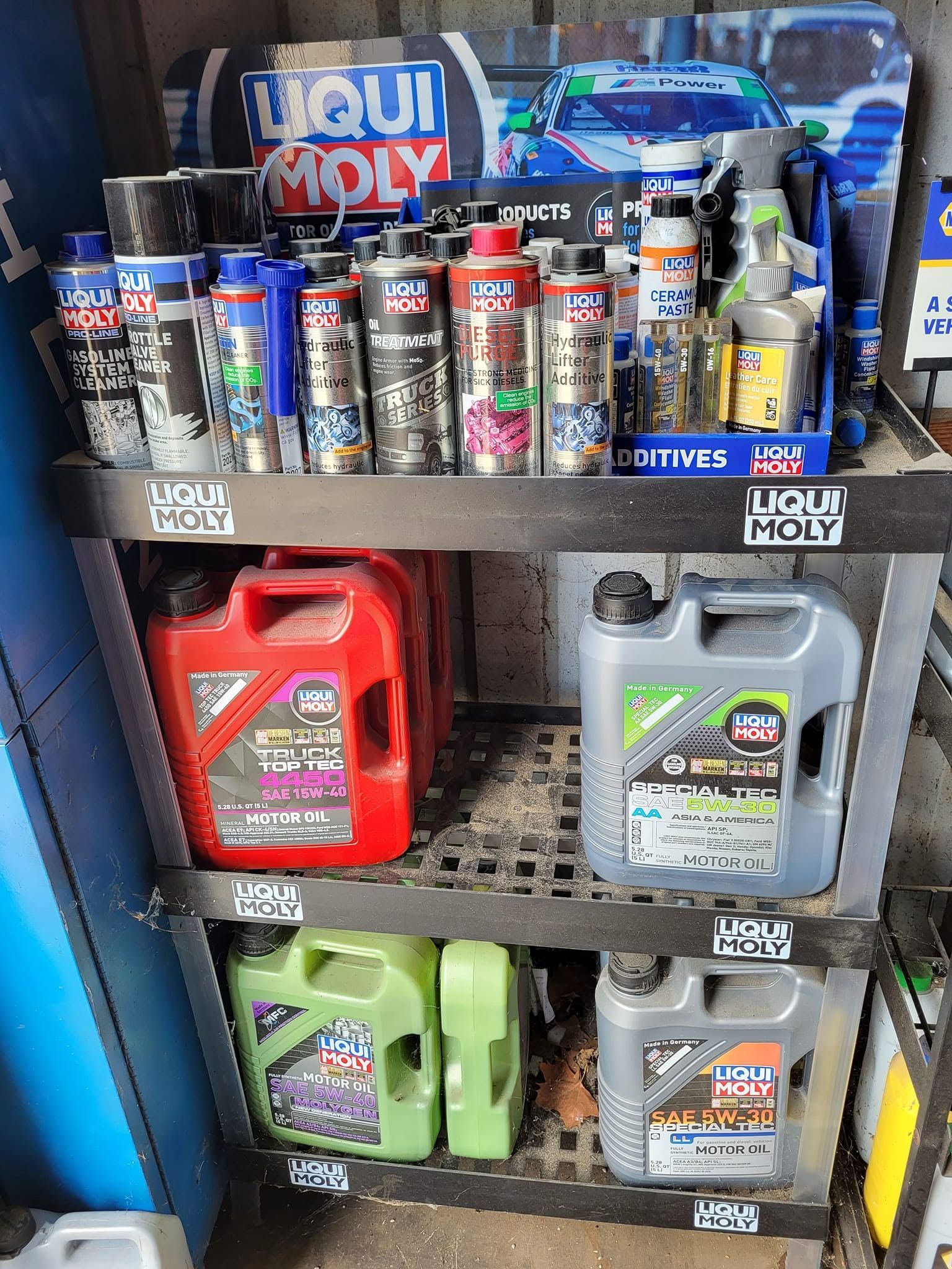 Metal shelf stocked with motor oil cans and plastic jugs in red, green, gray, and blue.