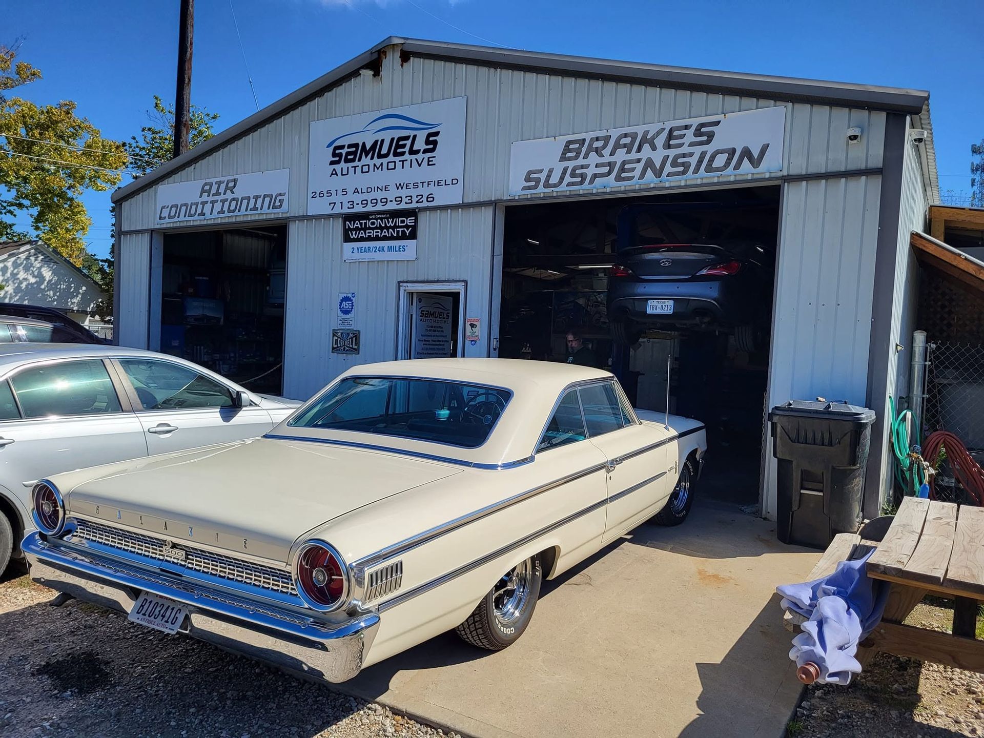 Classic white convertible parked outside a brake and suspension shop with garage bays open