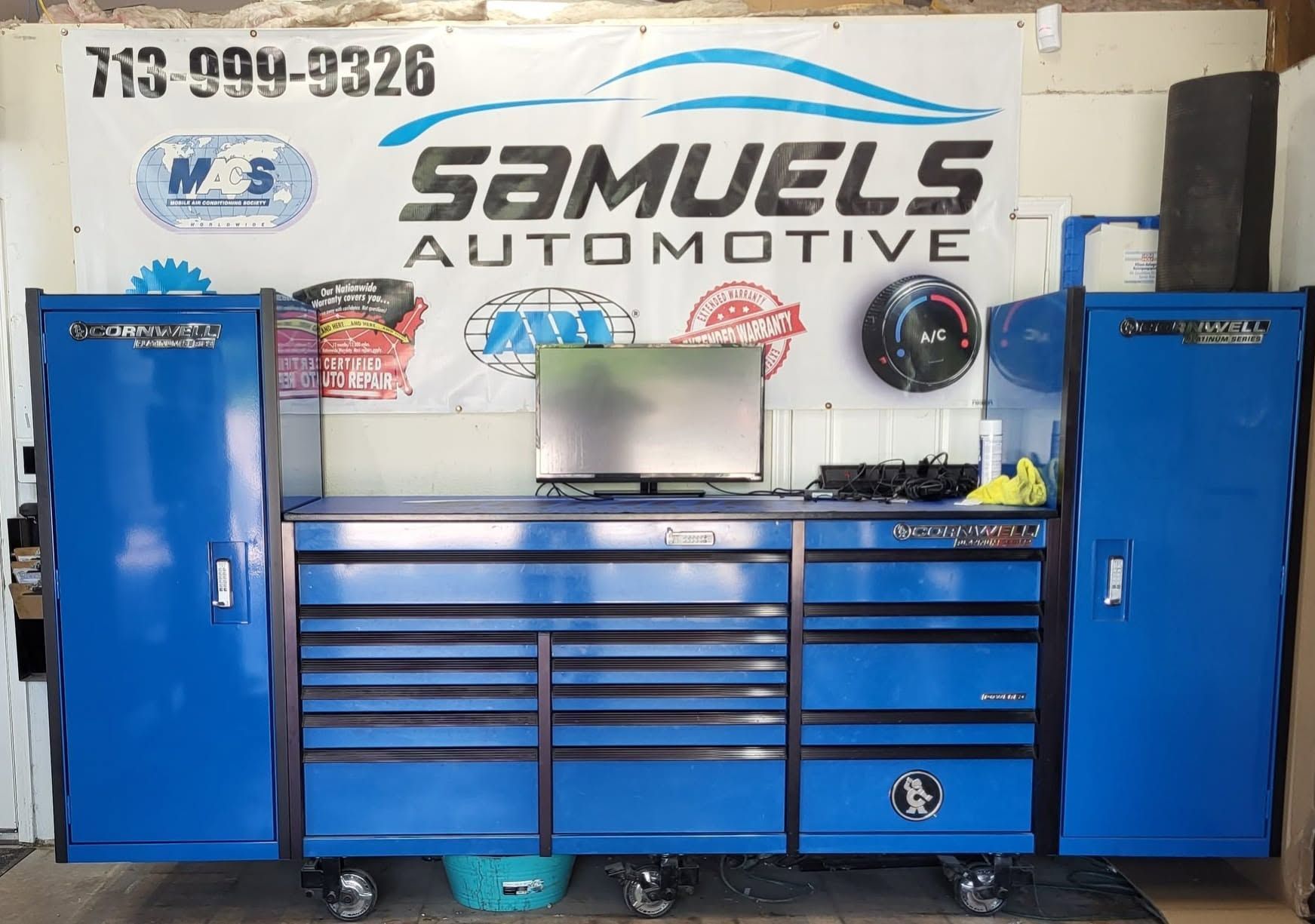Blue tool cabinets and workbench in an auto shop with a Samuels Automotive sign on the wall.